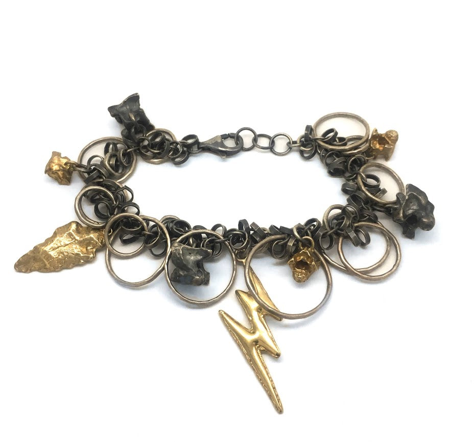 A bracelet composed of random sizes of round loops and links interspersed with gold and silver castings including an arrowhead, snake bones, and a lighting bolt